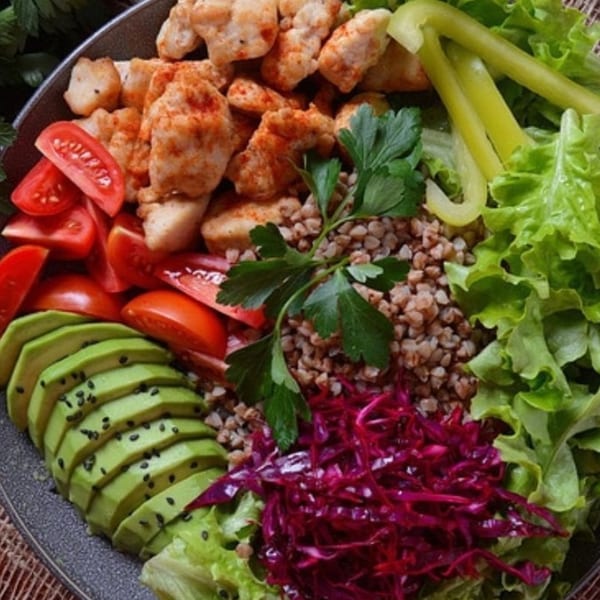 A healthy Leaf and Ginger bowl with chicken, avocado, tomatoes, red cabbage, and greens.