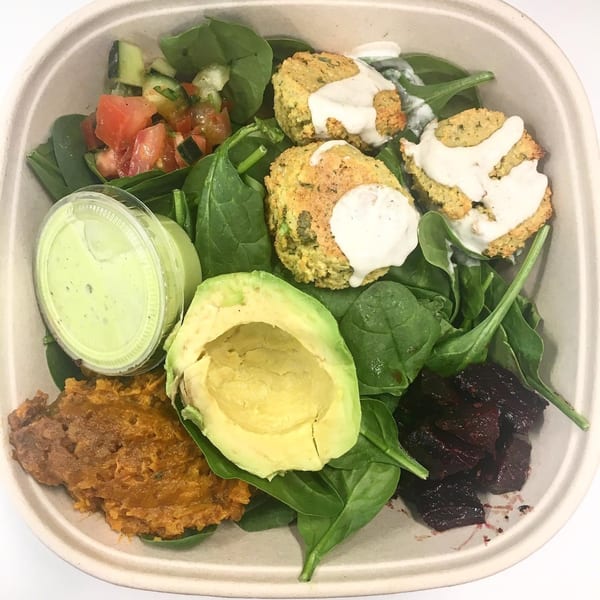 A healthy Leaf and Ginger bowl with falafel, avocado, spinach, salsa, and a side of dressing.